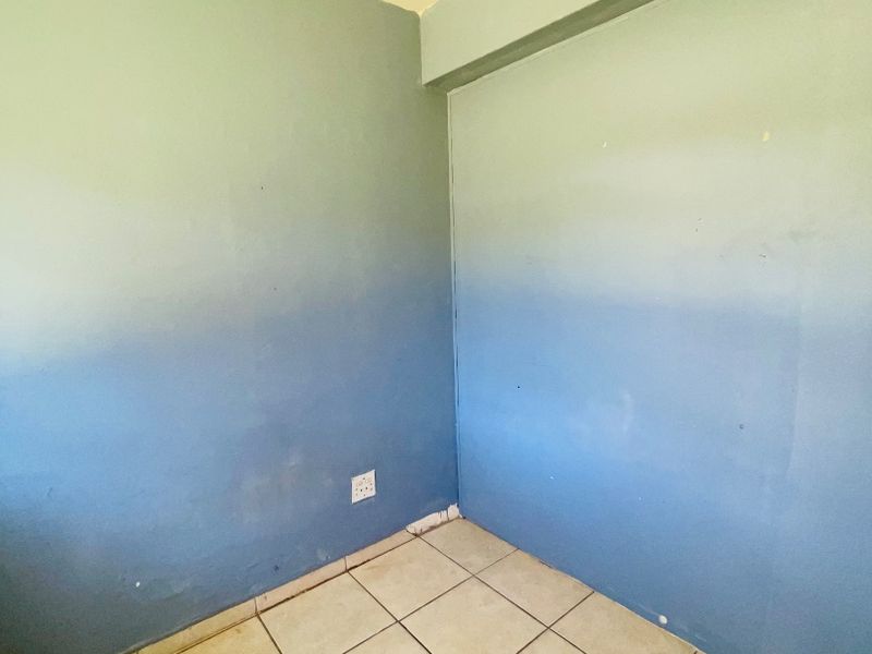 An empty bedroom featuring ceramic floor tiles and blue painted walls in need of cosmetic attention.