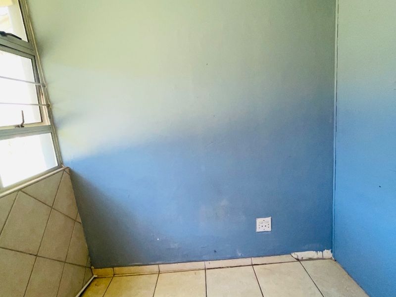 An empty bedroom featuring tiled flooring, blue painted walls, and an aluminium window frame, requiring minor cosmetic updates to improve its overall condition.