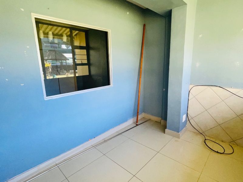 An empty living area featuring tiled flooring and a window, currently requiring minor cosmetic repairs to the walls and electrical finishing.