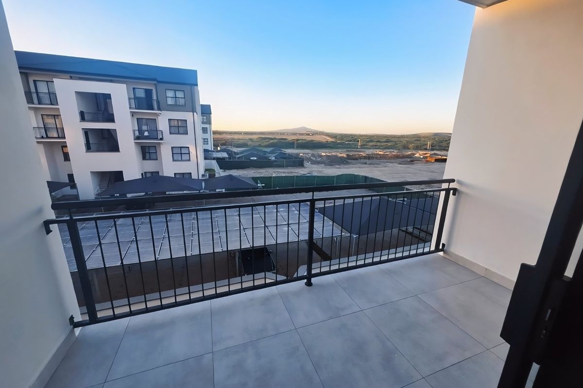 A clean, modern balcony featuring tiled flooring and a secure metal balustrade, offering an open view of the surrounding development area.