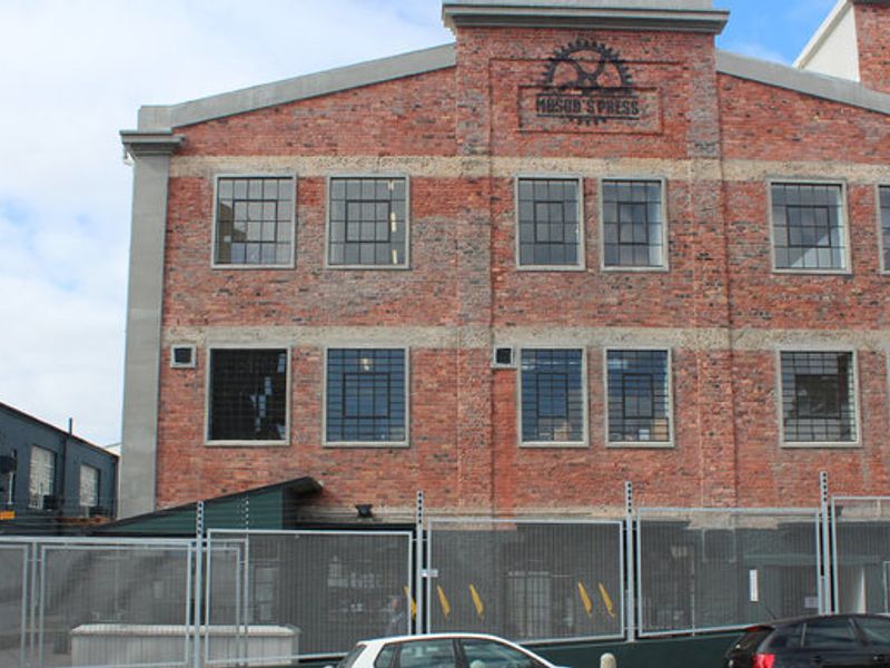 A multi-story commercial building featuring an exposed brick facade, industrial-style steel-framed windows, and secure perimeter fencing.