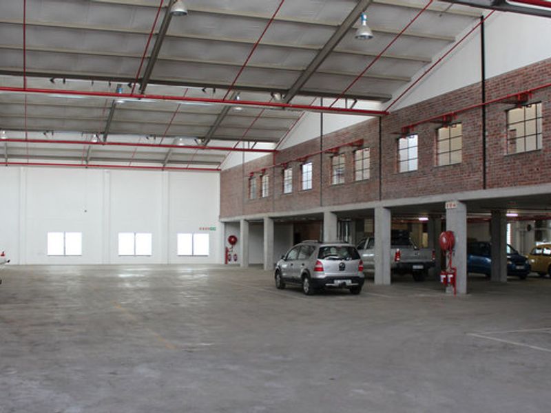 Spacious industrial-style commercial garage featuring exposed steel roof trusses, concrete flooring, and brickwork detailing with integrated sprinkler systems.