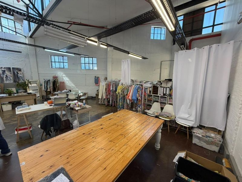 Spacious industrial-style open plan commercial studio featuring high ceilings with exposed trusses, large windows, and polished concrete floors, suitable for creative or retail use.