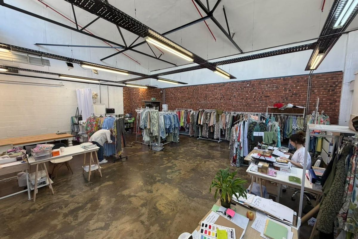 Spacious open-plan commercial studio featuring exposed brick walls, high ceilings with industrial steel trusses, and polished concrete flooring.