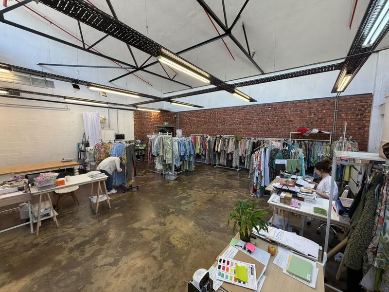 Spacious open-plan commercial studio featuring exposed brick walls, high ceilings with industrial steel trusses, and polished concrete flooring.