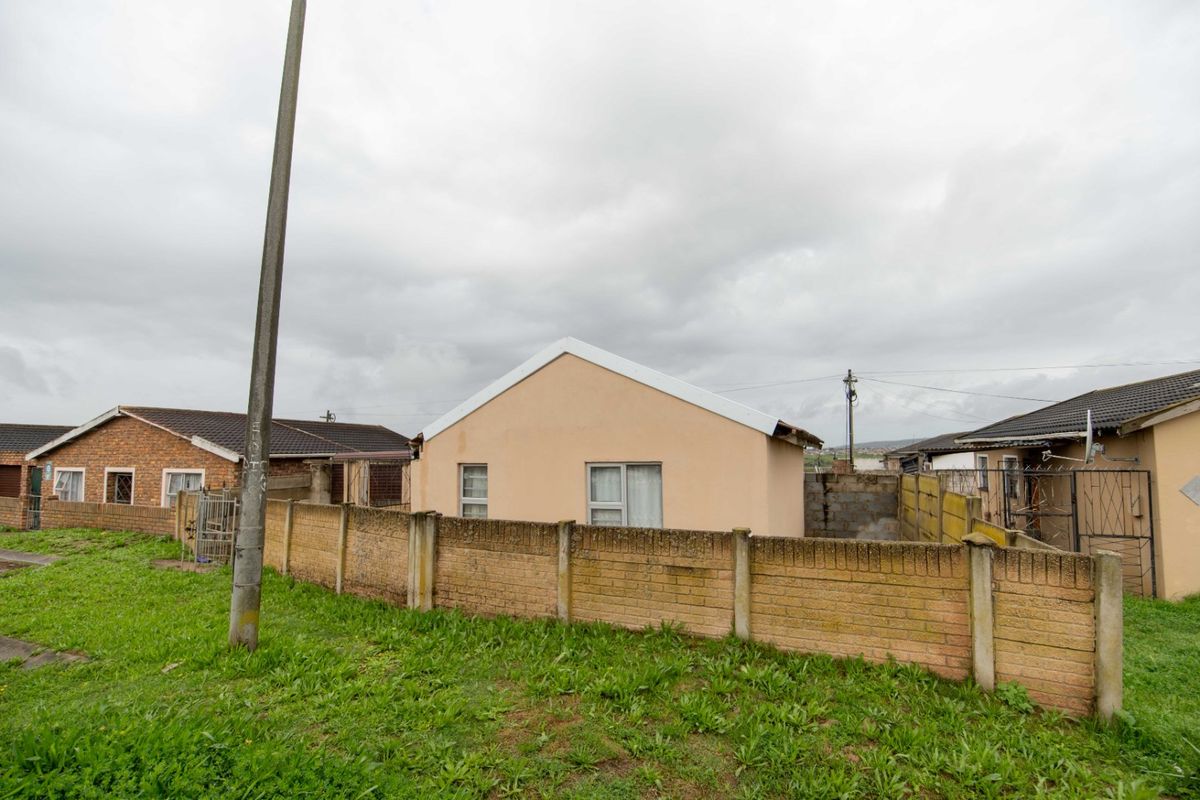 Rear view of a detached house featuring a perimeter brick wall, tiled roof, and aluminum window frames set within a residential neighborhood.