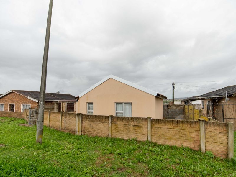 Rear view of a detached house featuring a perimeter brick wall, tiled roof, and aluminum window frames set within a residential neighborhood.