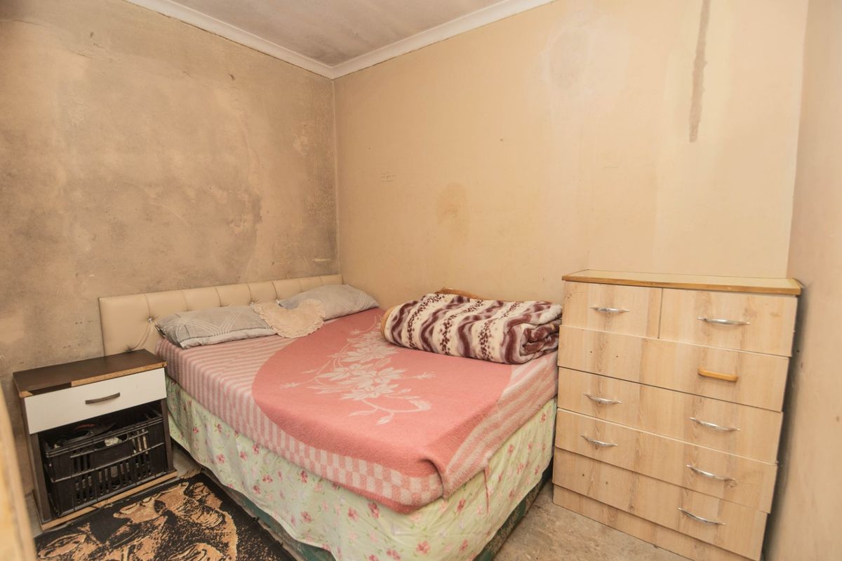 A bedroom featuring plain walls with visible surface damage and wear, requiring cosmetic attention and refurbishment.