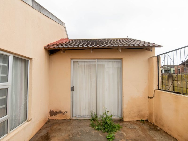 Rear exterior view of the property featuring a concrete patio area, sliding glass door access, and tiled roof section with visible maintenance requirements.