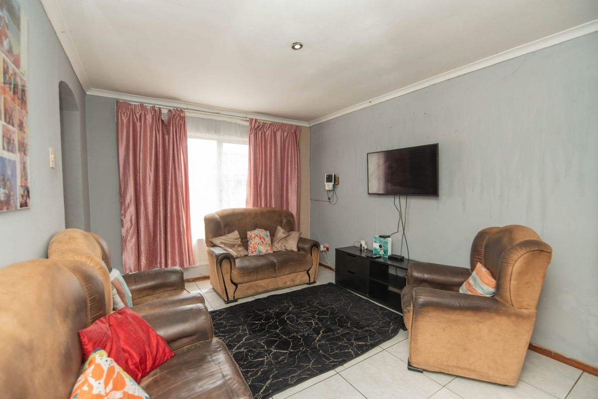 A living room featuring tiled flooring and recessed ceiling lighting, currently showing signs of wear on the wall surfaces.