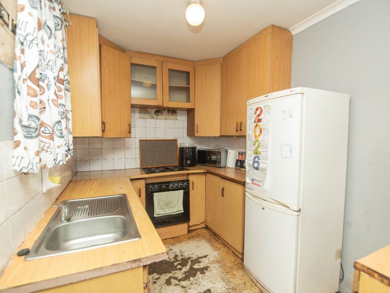 A compact kitchen featuring dated laminate cabinetry, a stainless steel sink, and built-in cooking appliances, requiring cosmetic updates to modernize the space.