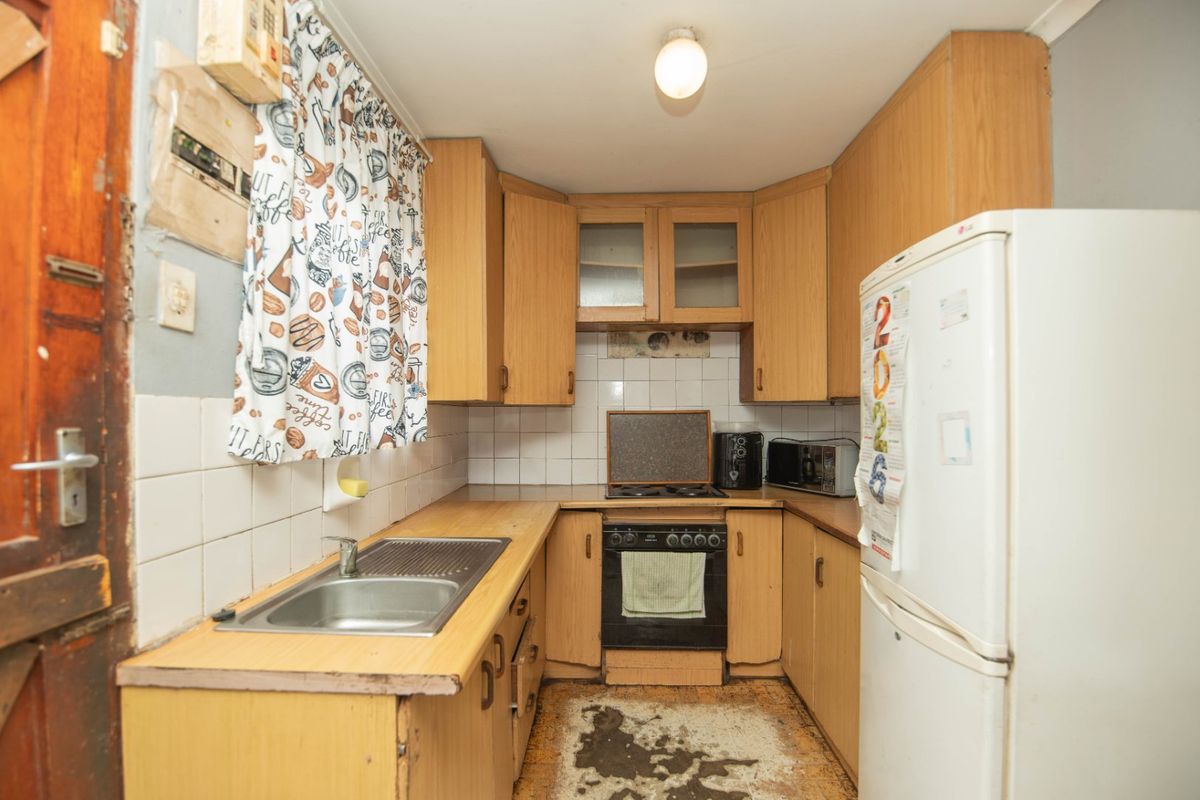 A compact kitchen featuring dated laminate cabinetry, a tiled backsplash, and a built-in oven, requiring cosmetic updates to modernize the space.
