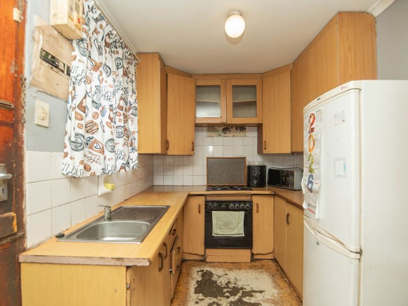 A compact kitchen featuring dated laminate cabinetry, a tiled backsplash, and a built-in oven, requiring cosmetic updates to modernize the space.