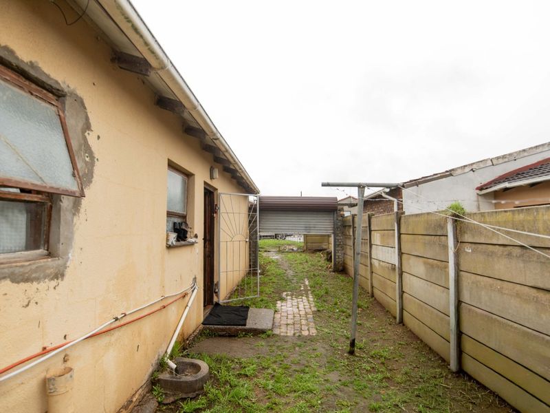 Rear exterior view of the property featuring a precast concrete boundary wall, paved pathway, and weathered exterior wall finish requiring maintenance.