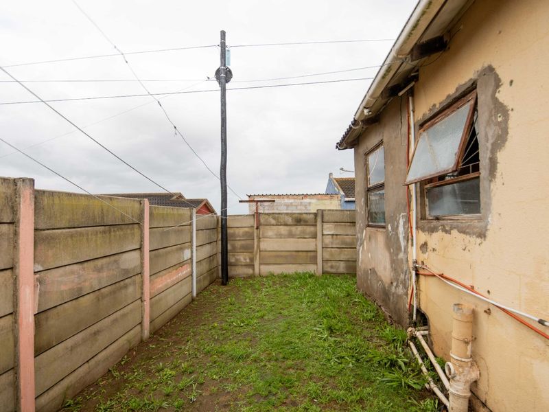 Rear exterior view of the property featuring a small garden area, precast concrete boundary walls, and visible exterior wall maintenance requirements.
