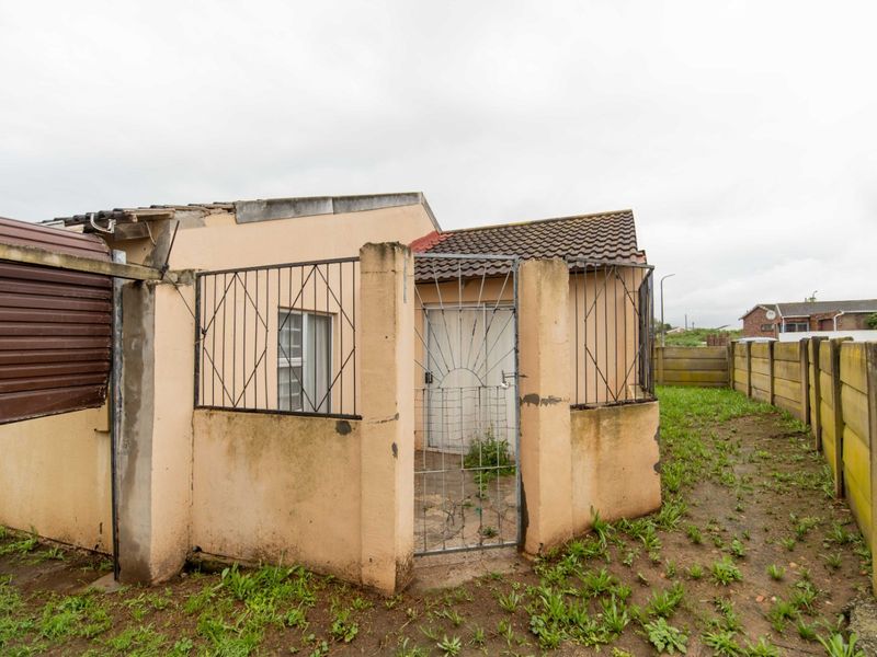 Front exterior view of a small house featuring security gates, bars, and a concrete boundary wall, showing signs of significant weathering and maintenance needs.