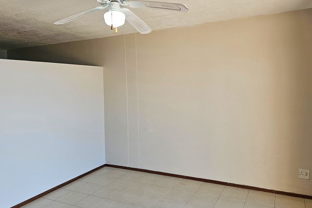 An empty living area featuring tiled flooring, a ceiling fan, and a partial room divider, offering a blank canvas for interior design.