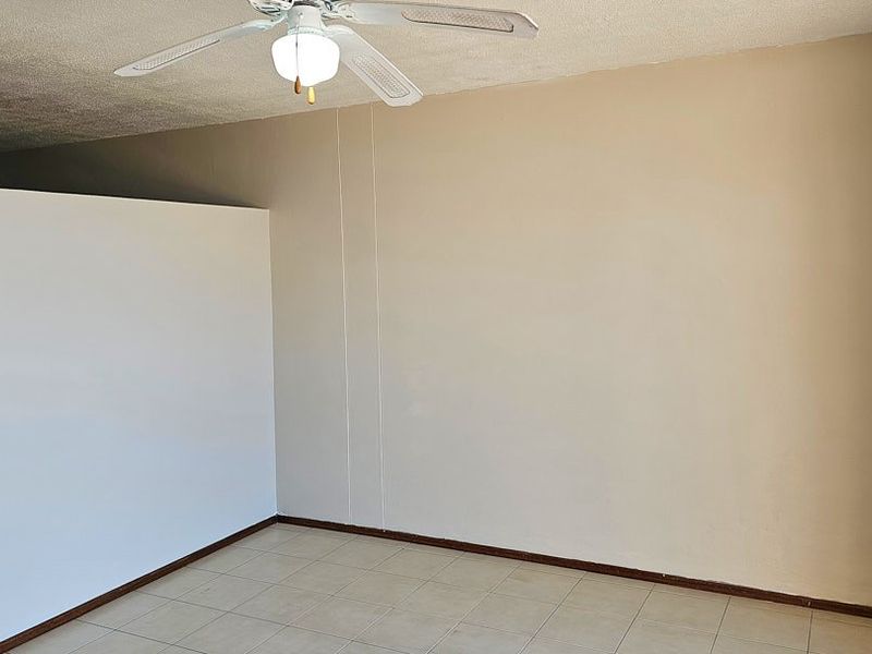 An empty living area featuring tiled flooring, a ceiling fan, and a partial room divider, offering a blank canvas for interior design.