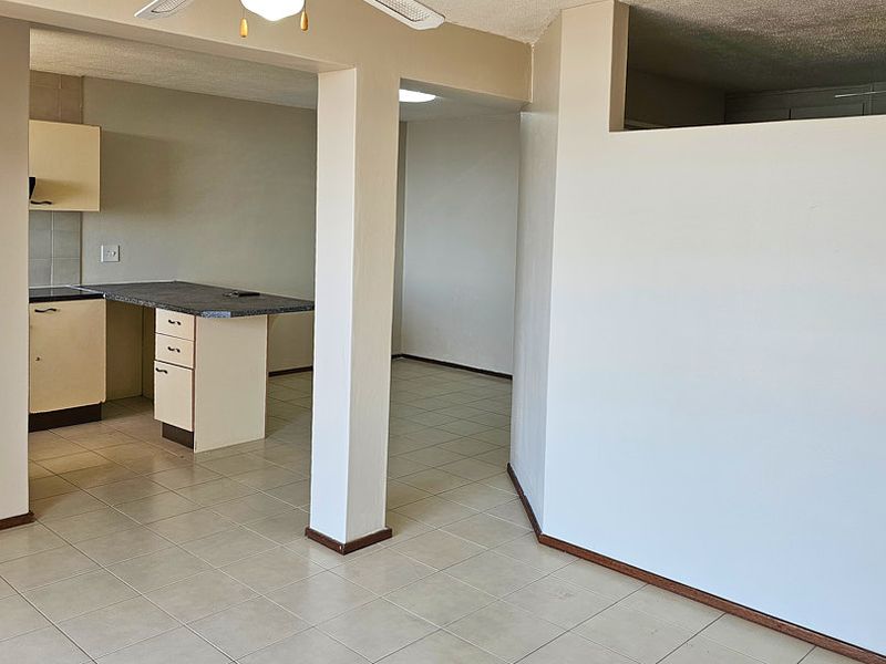 An open-plan living and kitchen area featuring tiled flooring, neutral walls, and functional kitchen cabinetry with a breakfast counter.
