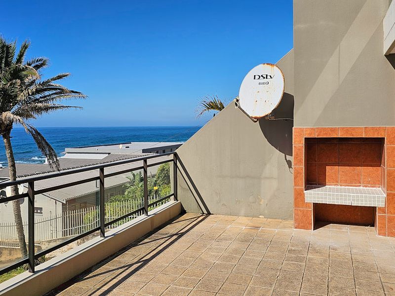 Spacious balcony featuring a built-in braai, tiled flooring, and a glass balustrade, offering stunning ocean views.