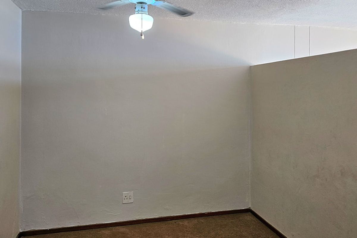 An empty bedroom featuring a ceiling fan, carpeted flooring, and neutral wall finishes, providing a blank canvas for personalization.