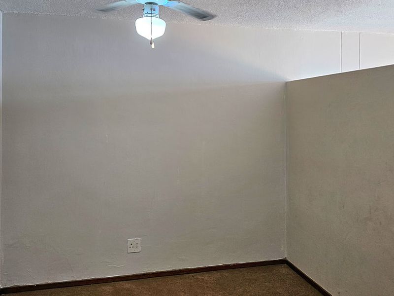 An empty bedroom featuring a ceiling fan, carpeted flooring, and neutral wall finishes, providing a blank canvas for personalization.