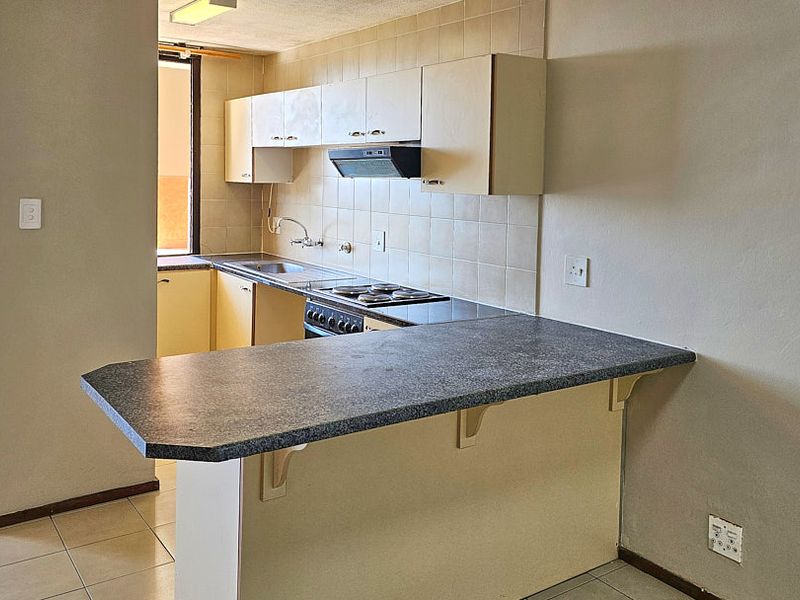 A functional kitchen featuring built-in cabinetry, a breakfast bar, and an integrated stove with an extractor fan, finished with tiled flooring and backsplash.