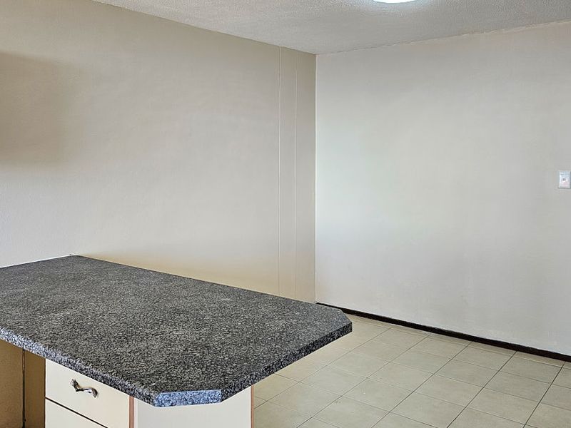 An empty kitchen area featuring neutral walls, tiled flooring, and a granite-topped breakfast counter, offering a clean canvas for potential updates.