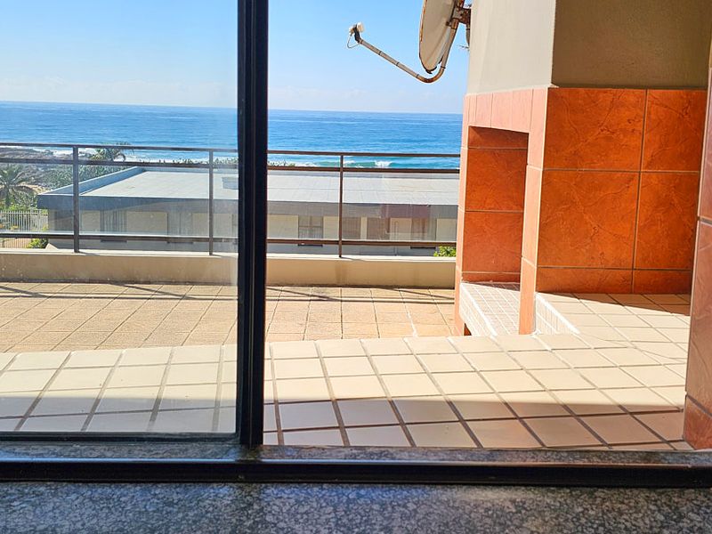 Spacious balcony featuring a built-in braai, tiled flooring, and a metal railing, offering clear views of the ocean.