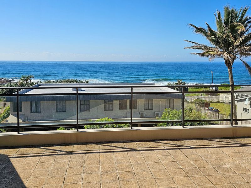 Spacious balcony featuring tiled flooring and a modern glass balustrade, offering expansive, unobstructed views of the ocean.