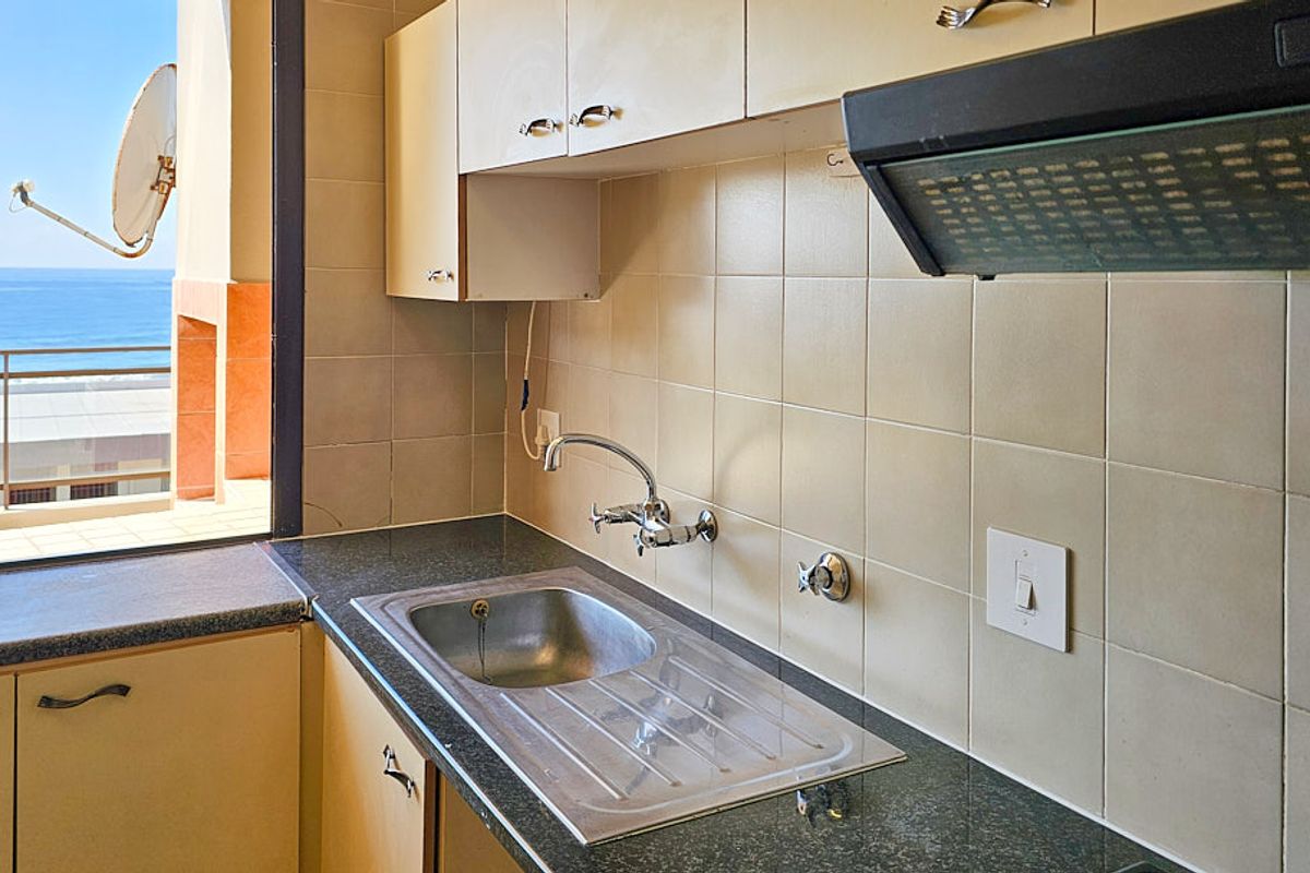 A functional kitchen area featuring built-in cabinetry, a stainless steel sink, and an extractor fan, with a view overlooking the ocean.