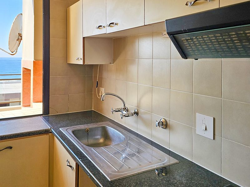 A functional kitchen area featuring built-in cabinetry, a stainless steel sink, and an extractor fan, with a view overlooking the ocean.