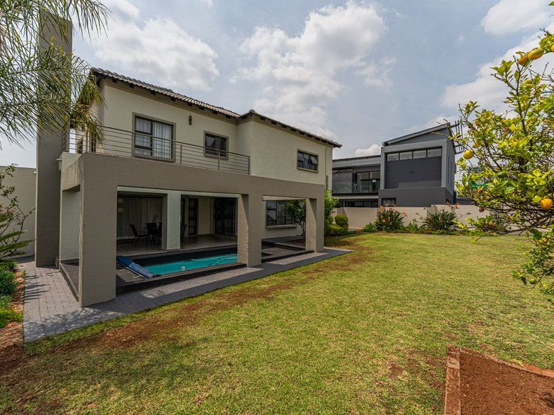 Rear view of the property featuring a covered patio, integrated swimming pool, balcony, and a well-maintained garden area.