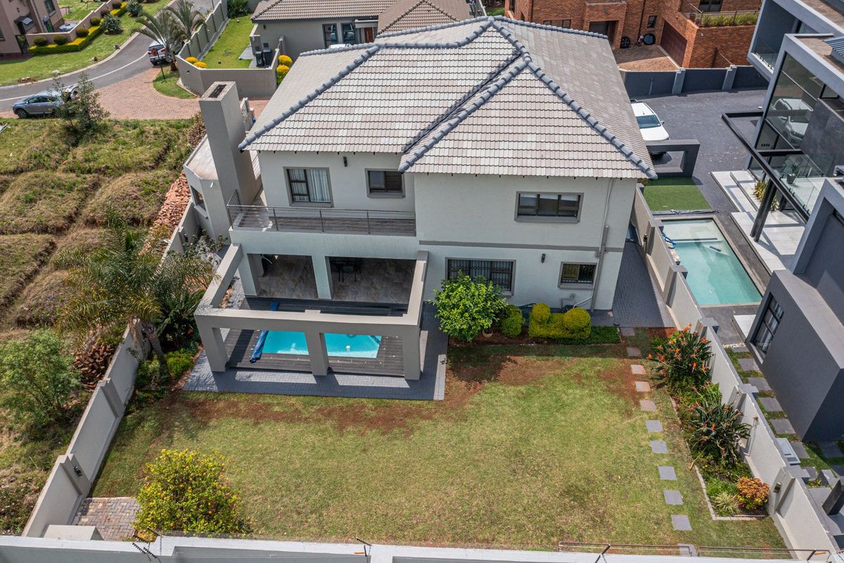 Aerial view of a two-story residential property featuring a tiled roof, swimming pool, covered patio, balcony, and a well-maintained garden.