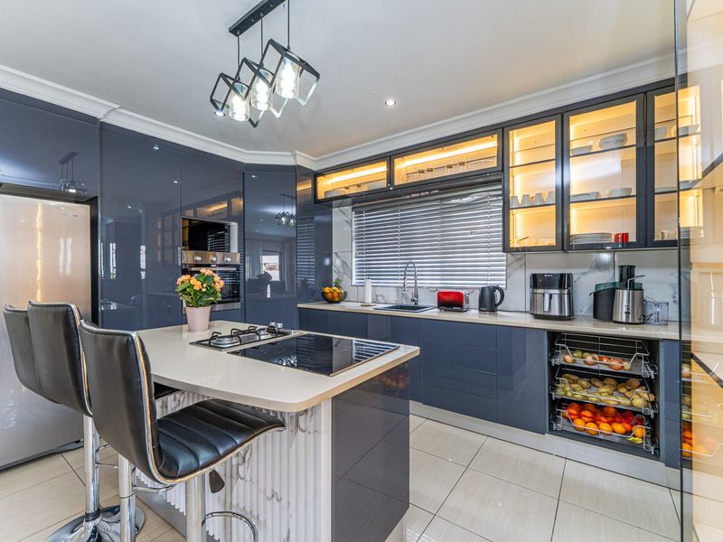 Modern kitchen featuring high-gloss cabinetry, stone countertops, a central island with a gas hob, and integrated lighting for a sleek, contemporary finish.