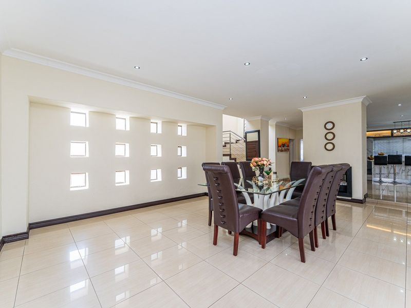 Spacious dining area featuring polished porcelain floor tiles, recessed downlighting, and a unique glass block feature wall, leading towards the staircase and kitchen.
