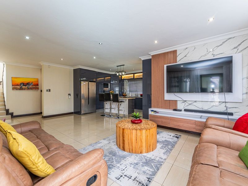Spacious open-plan living area featuring modern kitchen cabinetry, marble-effect feature wall with integrated media unit, and sleek porcelain floor tiles.