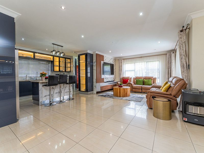 Spacious open-plan living area featuring polished porcelain tiles, a modern kitchen with island, and integrated display cabinetry with contemporary feature wall detailing.