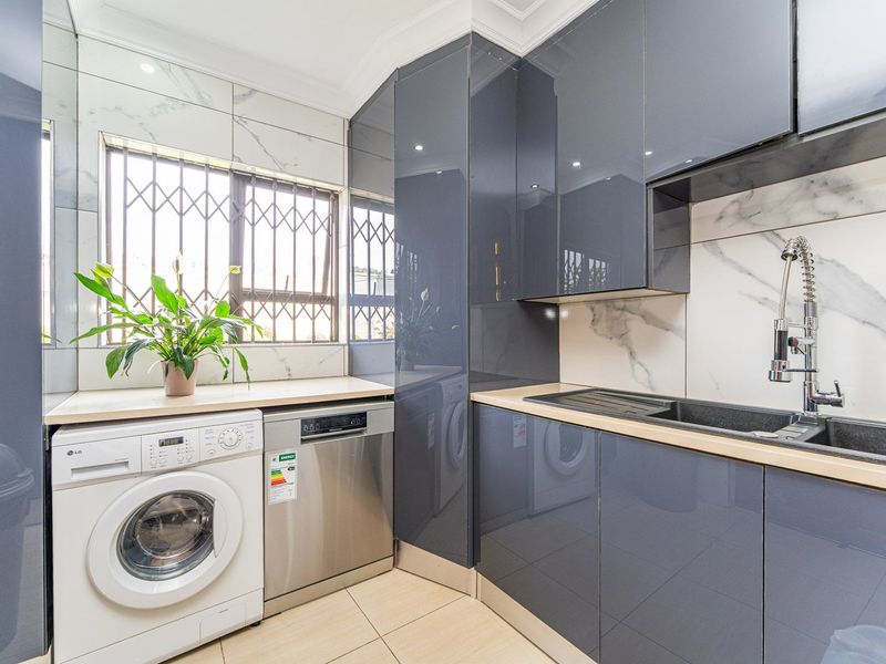 Modern laundry room featuring high-gloss grey cabinetry, marble-effect wall tiling, and a sleek undermount sink with a contemporary gooseneck faucet.