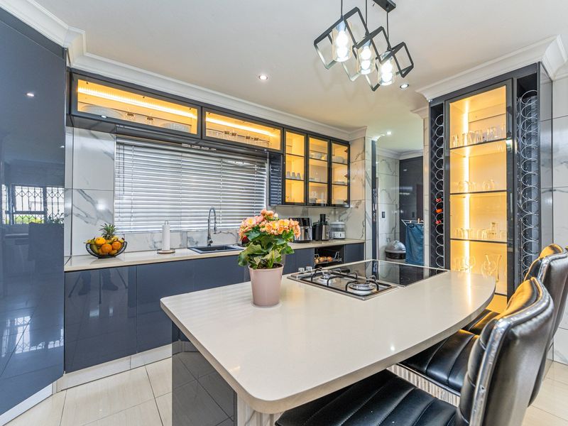 Modern kitchen featuring high-gloss cabinetry, stone countertops, integrated wine storage, gas hob, and elegant under-cabinet lighting with a sleek, contemporary finish.