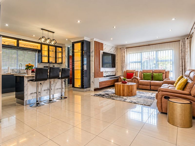 Modern open-plan living area featuring a sleek kitchen with island, marble-effect accents, built-in media unit, and polished tiled flooring throughout.