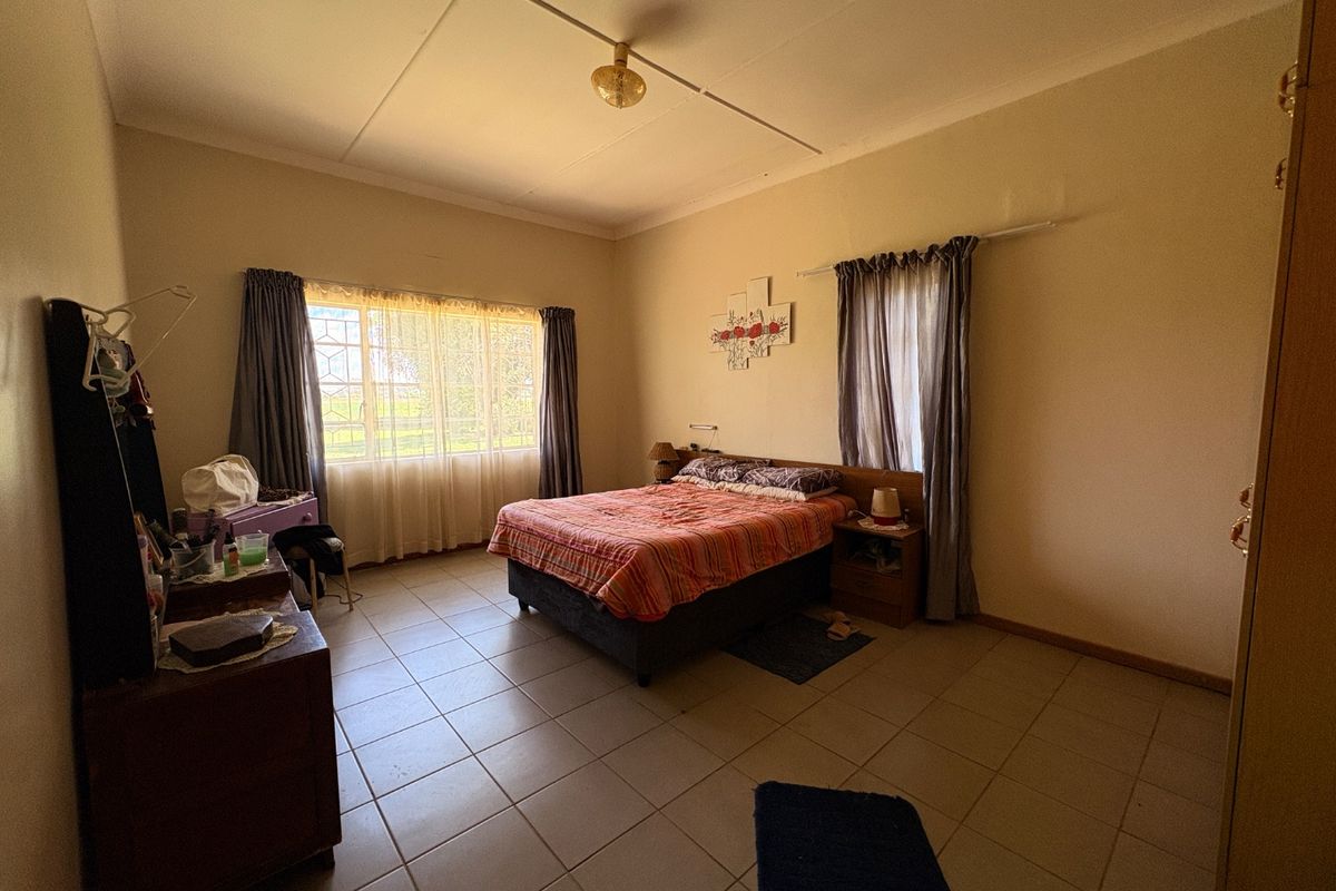 Spacious bedroom featuring tiled flooring, built-in storage, and large windows with security bars, offering a functional layout ready for cosmetic updates.