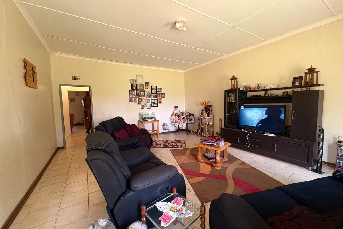 A spacious living room featuring tiled flooring and a panelled ceiling, offering a functional layout with access to adjacent rooms.