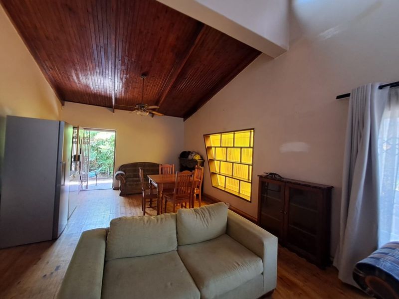 Spacious living area featuring a vaulted timber ceiling, unique glass block window, and direct access to the outdoor patio area.