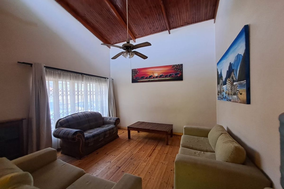 Spacious living room featuring a high vaulted timber ceiling with exposed beams, warm timber flooring, and a ceiling fan.