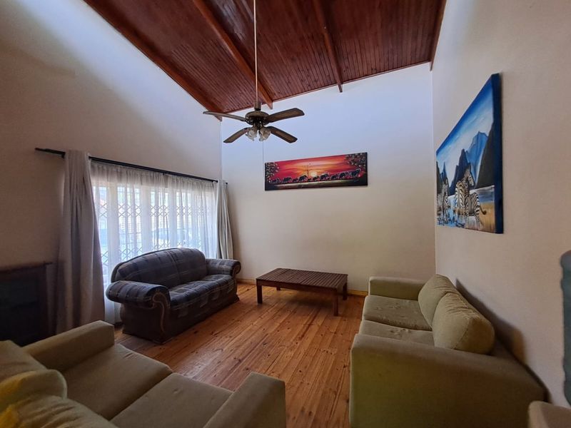 Spacious living room featuring a high vaulted timber ceiling with exposed beams, warm timber flooring, and a ceiling fan.