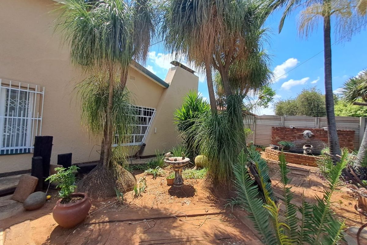 Rear garden area featuring established trees, a brick boundary wall, and a built-in water feature adjacent to the house exterior.