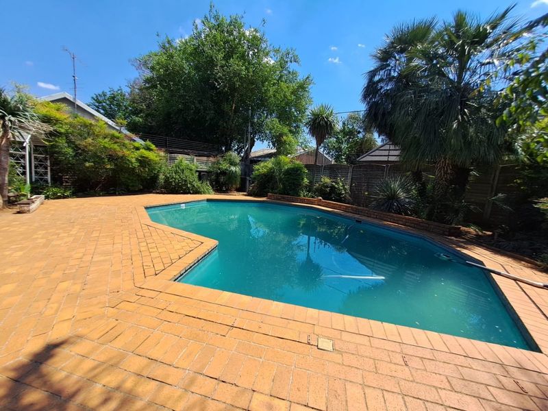 Outdoor pool area featuring a swimming pool surrounded by brick paving and established garden landscaping.