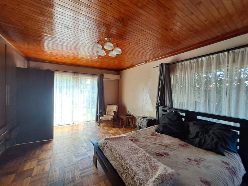 Spacious bedroom featuring classic parquet flooring, a warm wooden ceiling, built-in cupboards, and direct access to the garden through sliding glass doors.