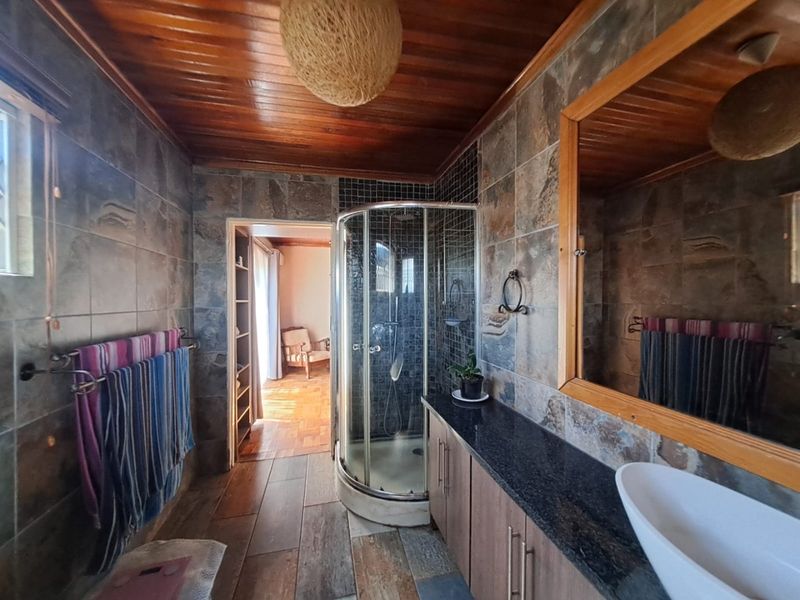 A bathroom featuring a corner shower, vanity with granite countertop, vessel sink, and timber-clad ceiling with natural stone wall tiling.